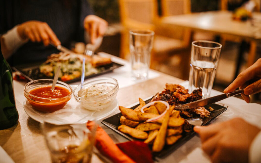 Table de restaurant avec deux personnes en train de manger. Les assiettes contiennent des frites belges, de la viande et de la salade, représentant un repas typique.