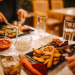 Table de restaurant avec deux personnes en train de manger. Les assiettes contiennent des frites belges, de la viande et de la salade, représentant un repas typique.