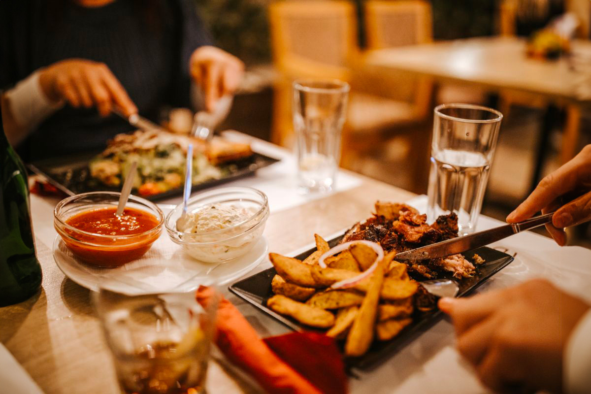 Table de restaurant avec deux personnes en train de manger. Les assiettes contiennent des frites belges, de la viande et de la salade, représentant un repas typique.